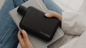 Memobottle A6 Edelstahl in Schwarz liegt flach auf einem Notizbuch auf dem Schoss