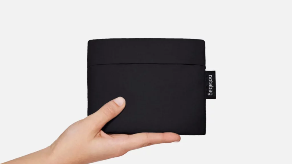 Notabag Original gefaltet im angenähten Beutel mit Notabag-Label in einer Hand