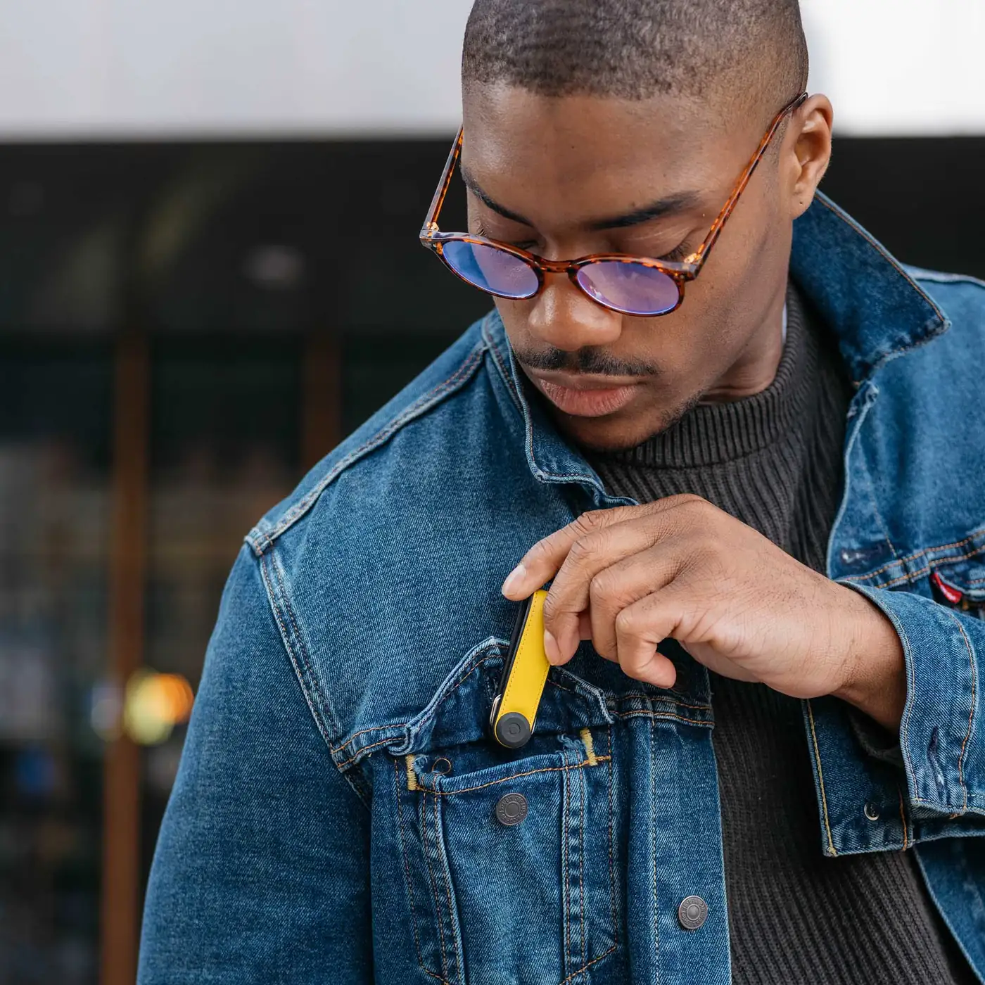 Mann steckt einen gelben Orbitkey Key Organiser Hybrid Leather in die Brusttasche einer Jeansjacke