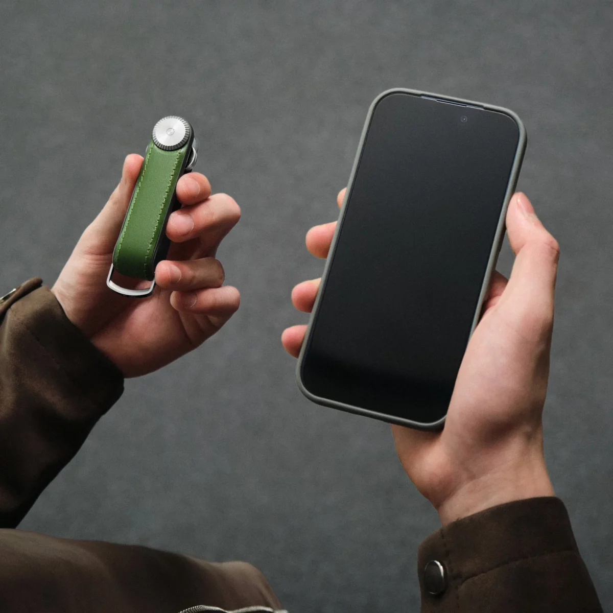 Orbitkey Key Organiser Tracker Leder in Waldgrün in der einen Hand, Smartphone zum Orten der Schlüssel in der anderen
