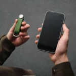Orbitkey Key Organiser Tracker Leder in Waldgrün in der einen Hand, Smartphone zum Orten der Schlüssel in der anderen