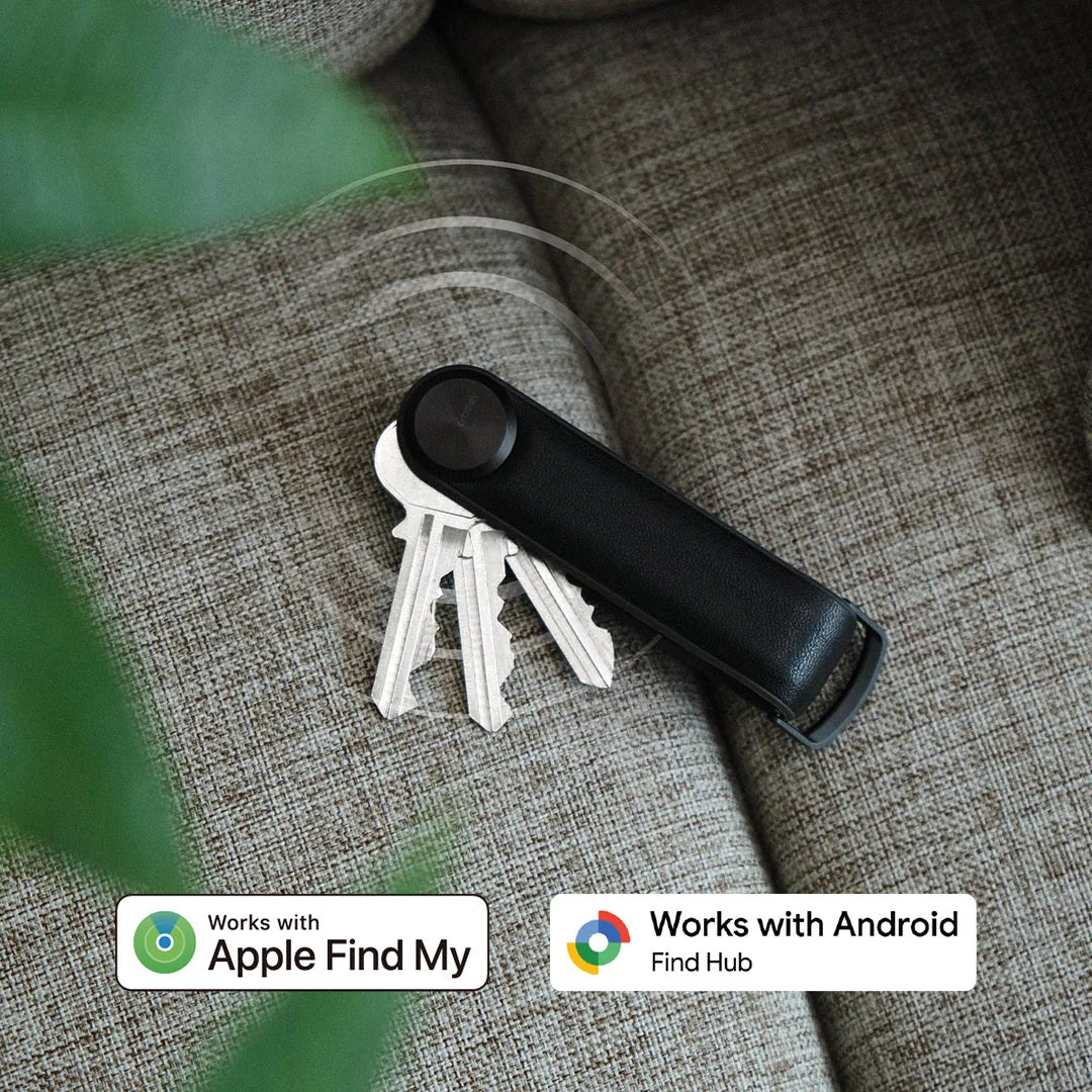 Orbitkey Key Organiser Tracker in Schwarz auf einem Sofa, mit Hinweis auf Apple «Wo ist?» und Google Find Hub