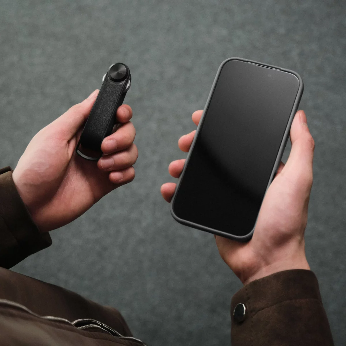 Orbitkey Key Organiser Tracker in Schwarz in der einen Hand, Smartphone zum Orten der Schlüssel in der anderen