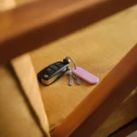 Orbitkey Universal Tracker in Lila am Schlüsselring mit Autoschlüssel und Hausschlüsseln auf einer Holzbank