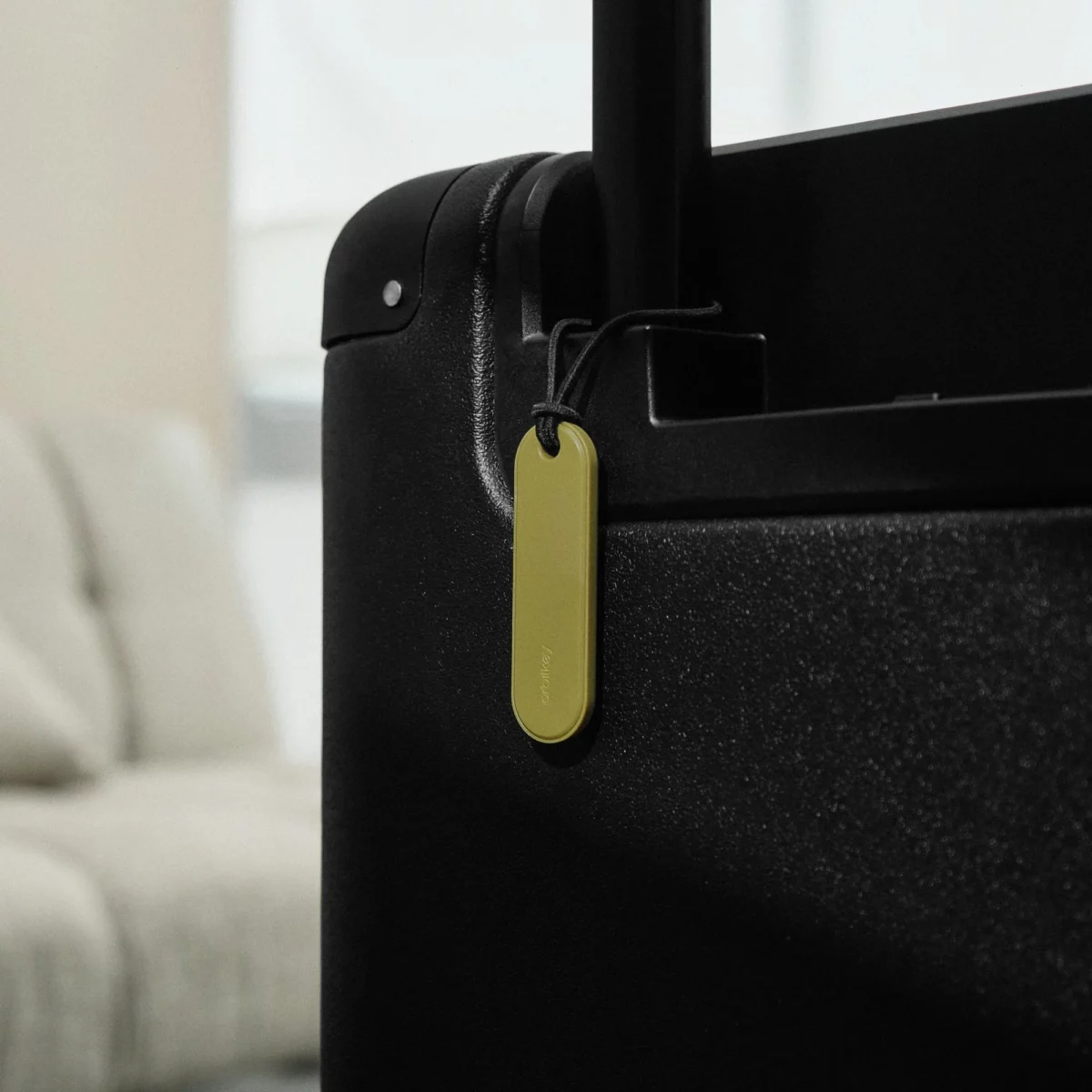 Orbitkey Universal Tracker in Pistazie hängt am Griff eines schwarzen Koffers, damit das Gepäck auffindbar bleibt
