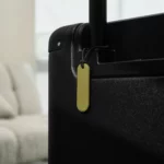 Orbitkey Universal Tracker in Pistazie hängt am Griff eines schwarzen Koffers, damit das Gepäck auffindbar bleibt