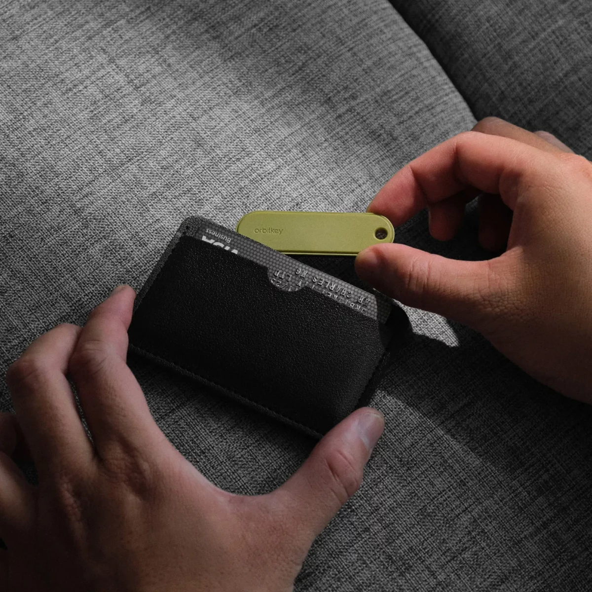 Hand schiebt den flachen Orbitkey Universal Tracker in Pistazie in ein schwarzes Kartenetui