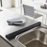 Yamazaki Abtropfmatte TOWER faltbar in Schwarz, aufgerollt auf der Arbeitsplatte neben dem Becken