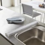 Yamazaki Abtropfmatte TOWER faltbar in Weiss, aufgerollt auf der Arbeitsplatte neben dem Becken