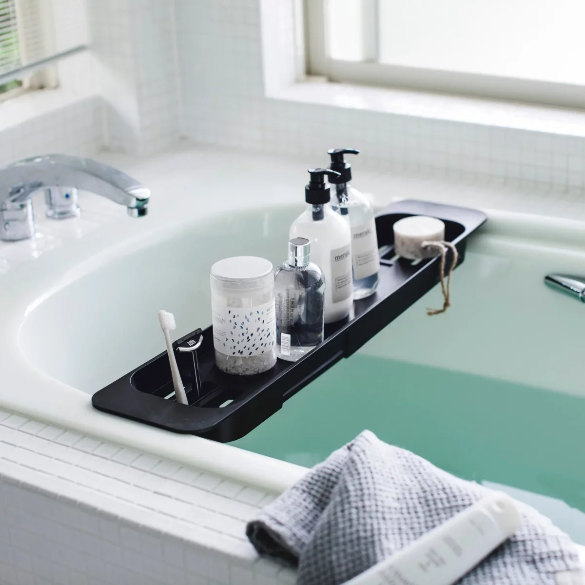 Porte-objets extensible TOWER de Yamazaki, noir, posé sur la baignoire avec des bouteilles et une brosse à dents