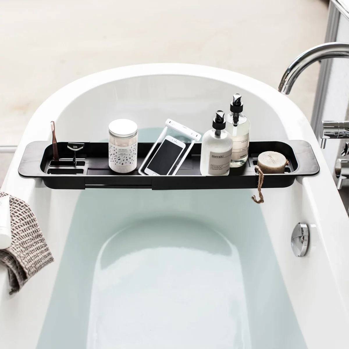 Porte-objets de baignoire Yamazaki TOWER, extensible, noir, avec un smartphone dans son étui de protection et des produits de soin