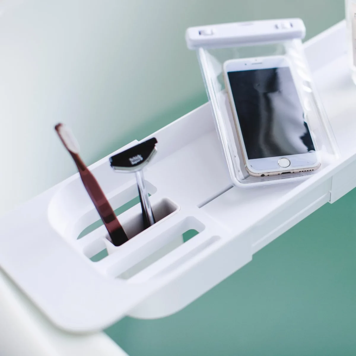 Porte-objets de baignoire Yamazaki TOWER extensible, blanc ; gros plan sur les compartiments avec une brosse à dents et un smartphone