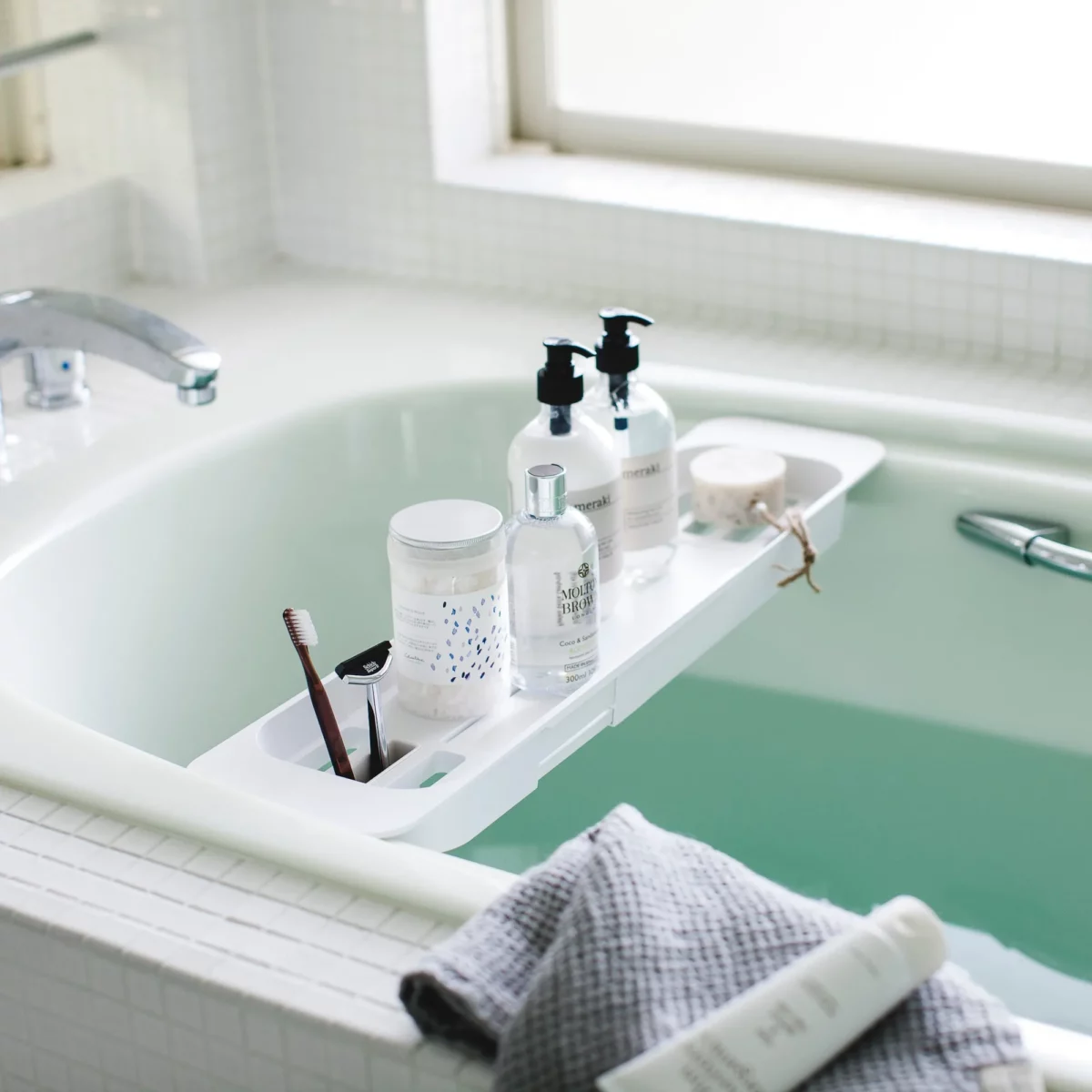 Porte-objets extensible TOWER de Yamazaki, blanc, posé sur la baignoire avec des bouteilles et une brosse à dents