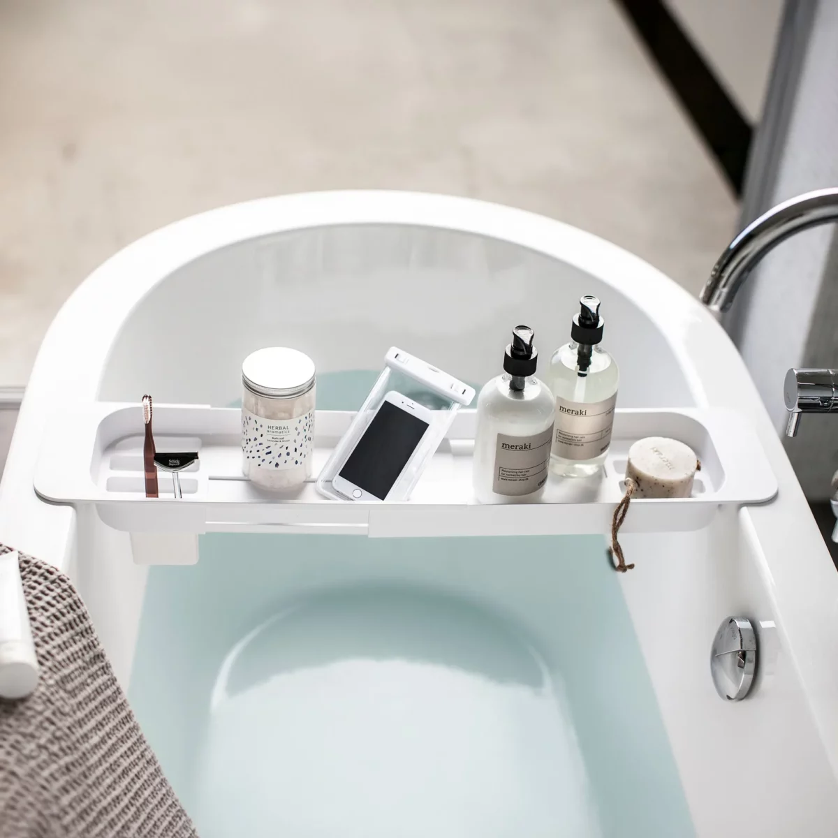 Porte-objets de baignoire Yamazaki TOWER extensible, blanc, avec un smartphone dans son étui de protection et des produits de soin