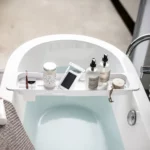Porte-objets de baignoire Yamazaki TOWER extensible, blanc, avec un smartphone dans son étui de protection et des produits de soin