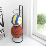 Yamazaki FRAME Ball Stand in black, with a volleyball and a basketball in the corner of the room by the window