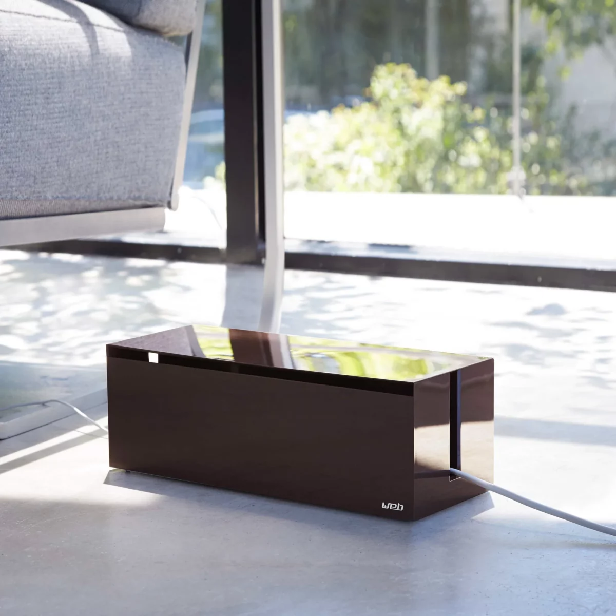 Yamazaki Cable Box WEB in Braun, am Boden neben dem Sofa vor dem Fenster, Kabel seitlich