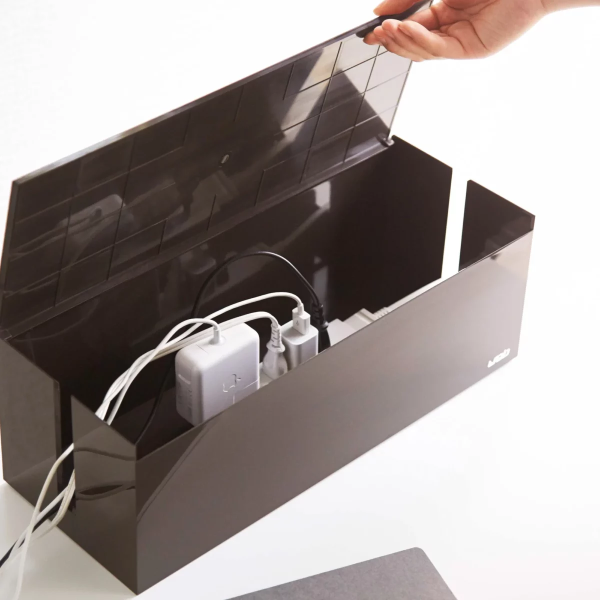 Yamazaki Cable Box WEB in Braun, Hand hebt den Deckel, darin Steckerleiste und Netzteile