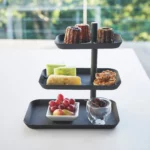 Yamazaki Etagere TOWER 3-stöckig drehbar in Schwarz, von vorne vor dem Fenster mit Früchten und Törtchen