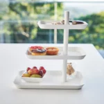Yamazaki Etagere TOWER 3-stöckig drehbar in Weiss, von vorne vor dem Fenster mit Früchten und Törtchen