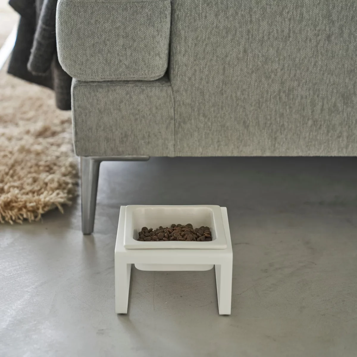 Yamazaki TOWER Food Bowl, single, with stand in white, on the concrete floor next to the sofa with food