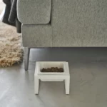 Yamazaki TOWER Food Bowl, single, with stand in white, on the concrete floor next to the sofa with food