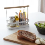Étagère à épices Yamazaki TOSCA avec poignée en bois, de couleur blanche, posée sur la table à manger avec des bouteilles, à côté du pain et de la salade