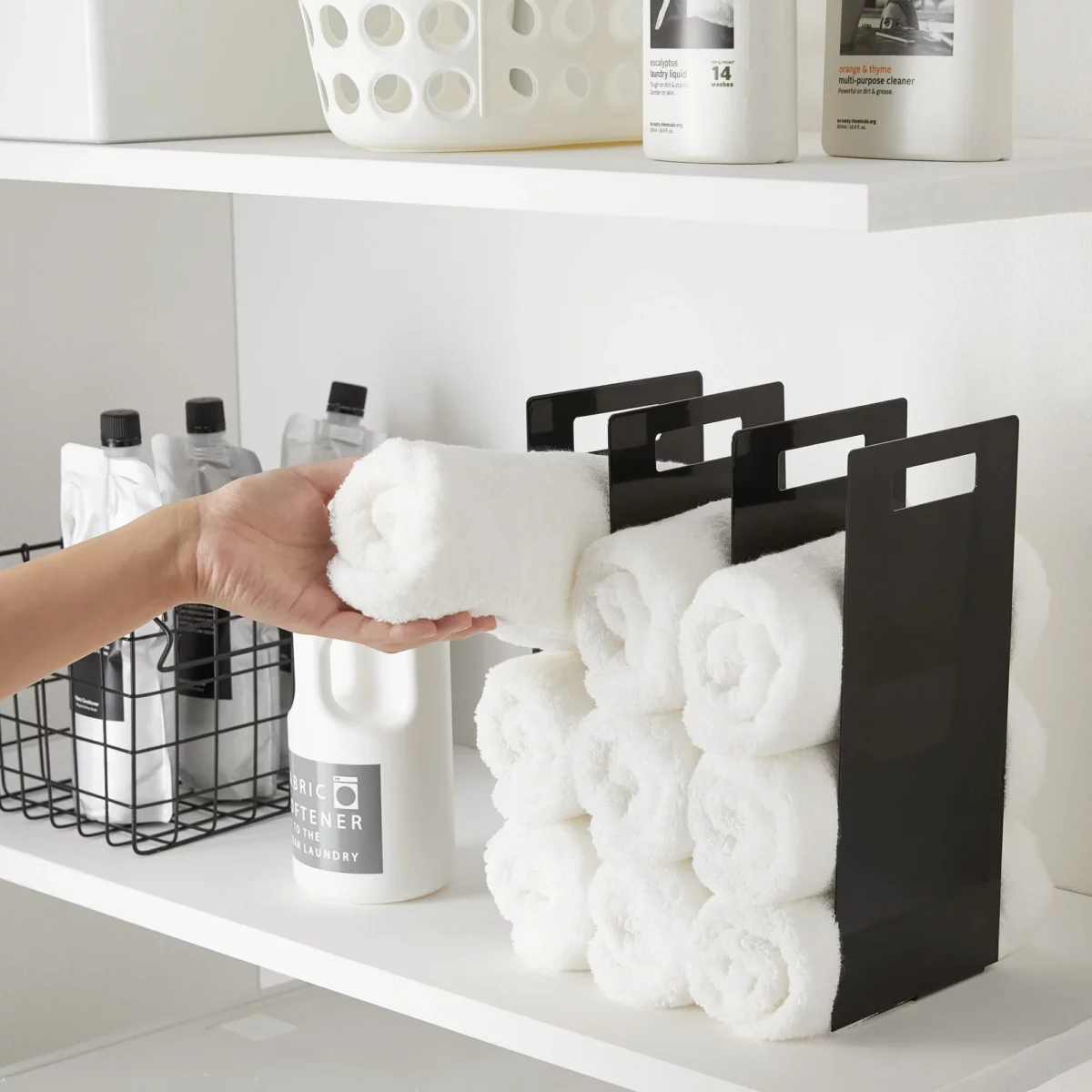 Yamazaki TOWER Towel Storage, Set of 2 in Black; a hand places a rolled-up towel into the compartment