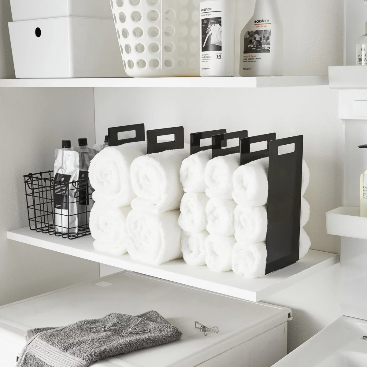 Yamazaki TOWER Towel Storage, Set of 2 in Black, on the shelf next to the laundry detergent and wire basket, wide view