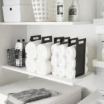 Yamazaki TOWER Towel Storage, Set of 2 in Black, on the shelf next to the laundry detergent and wire basket, wide view