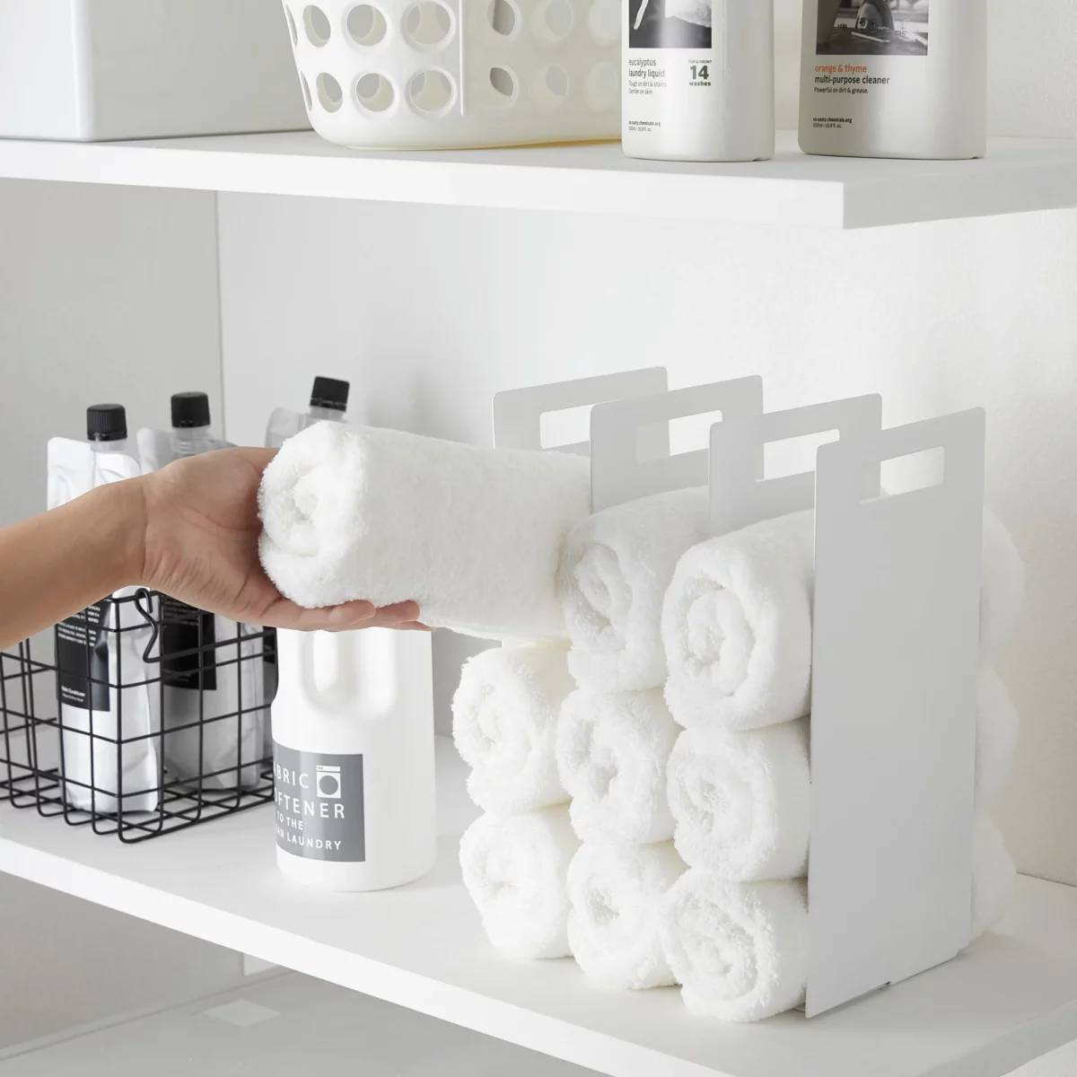 Yamazaki TOWER Towel Storage, Set of 2 in White; a hand is placing a rolled-up towel into the compartment