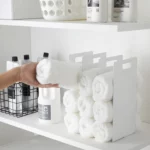 Yamazaki TOWER Towel Storage, Set of 2 in White; a hand is placing a rolled-up towel into the compartment