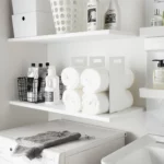 Yamazaki TOWER Towel Storage, Set of 2 in White, on the shelf next to the laundry detergent and wire basket, wide view