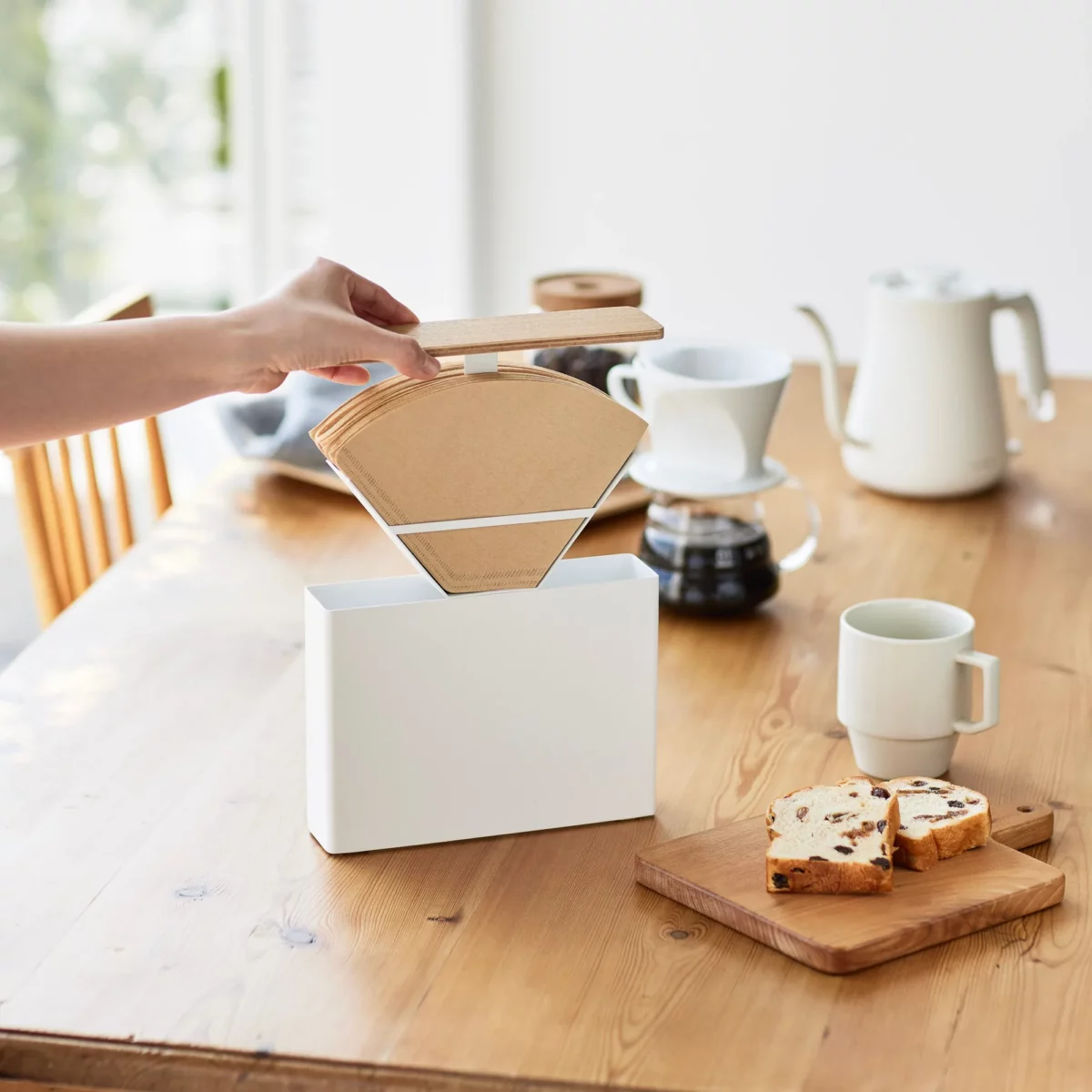Yamazaki Kaffeefilterbox TOSCA mit Holzdeckel in Weiss, Hand nimmt einen Kaffeefilter aus der offenen Box