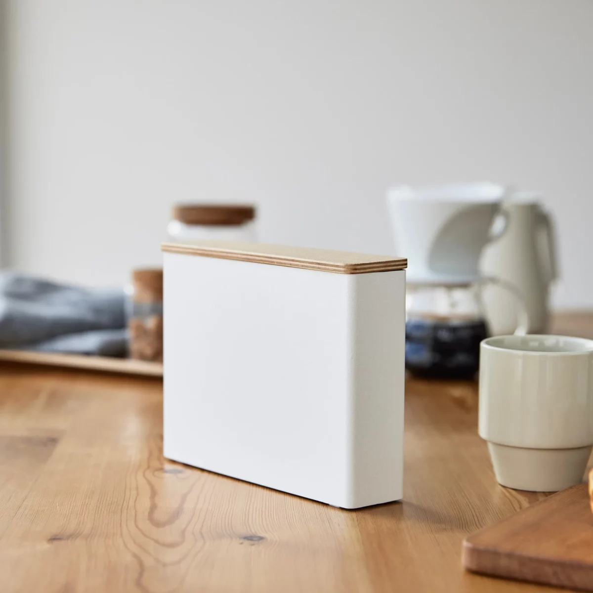 Yamazaki Kaffeefilterbox TOSCA mit Holzdeckel in Weiss, auf dem Holztisch neben Tasse und Wasserkocher