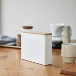 Yamazaki Kaffeefilterbox TOSCA mit Holzdeckel in Weiss, auf dem Holztisch neben Tasse und Wasserkocher