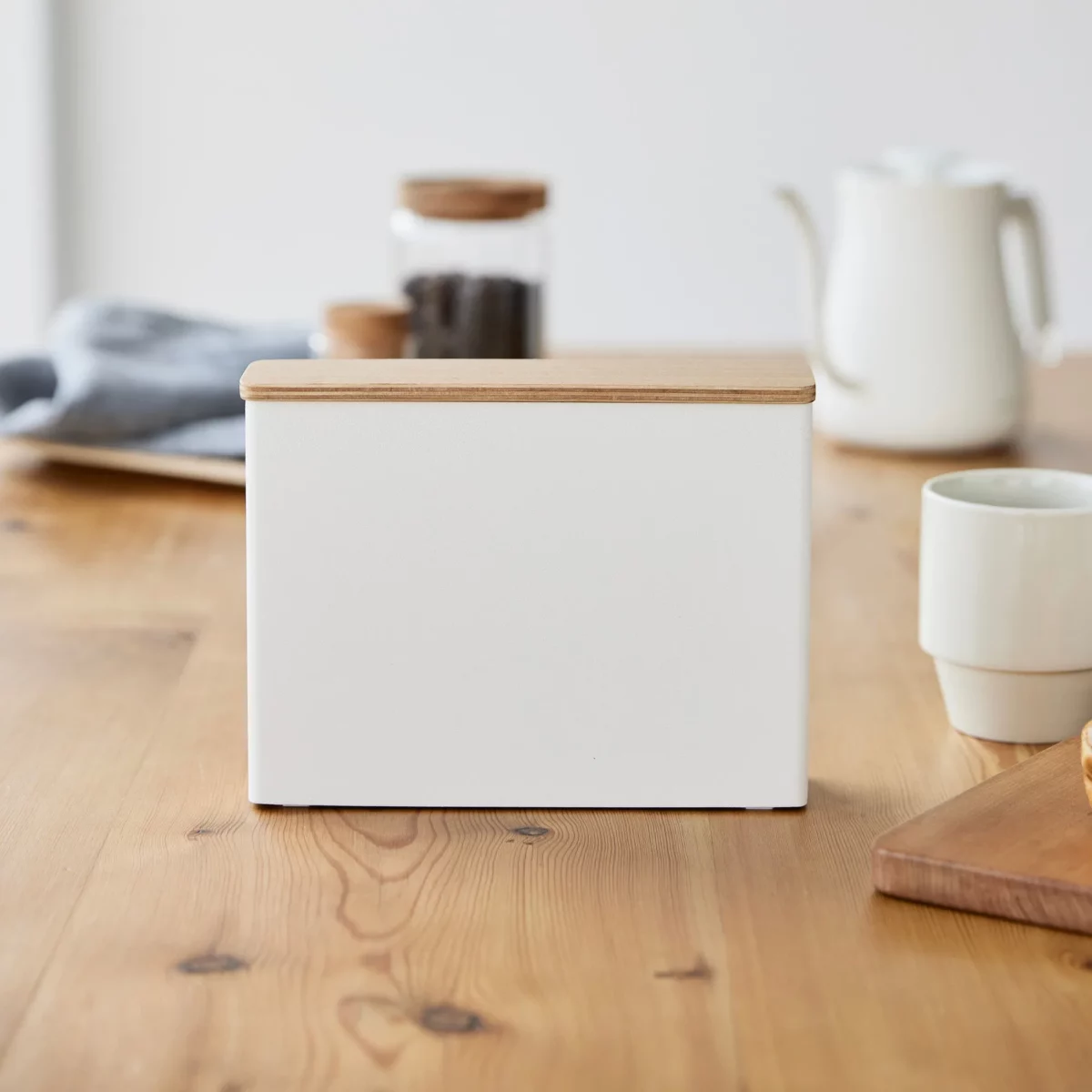 Yamazaki Kaffeefilterbox TOSCA mit Holzdeckel in Weiss, von vorne auf dem Esstisch neben einer Tasse