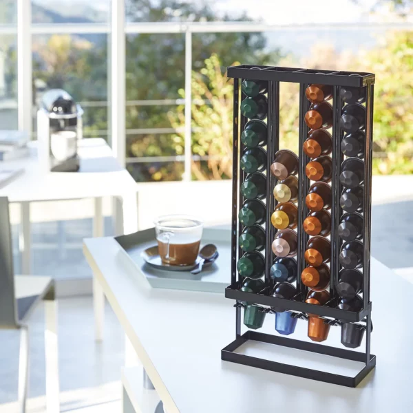 Porte-capsules à café Yamazaki « TOWER » en noir, avec des capsules colorées à côté d'une tasse d'expresso près de la fenêtre