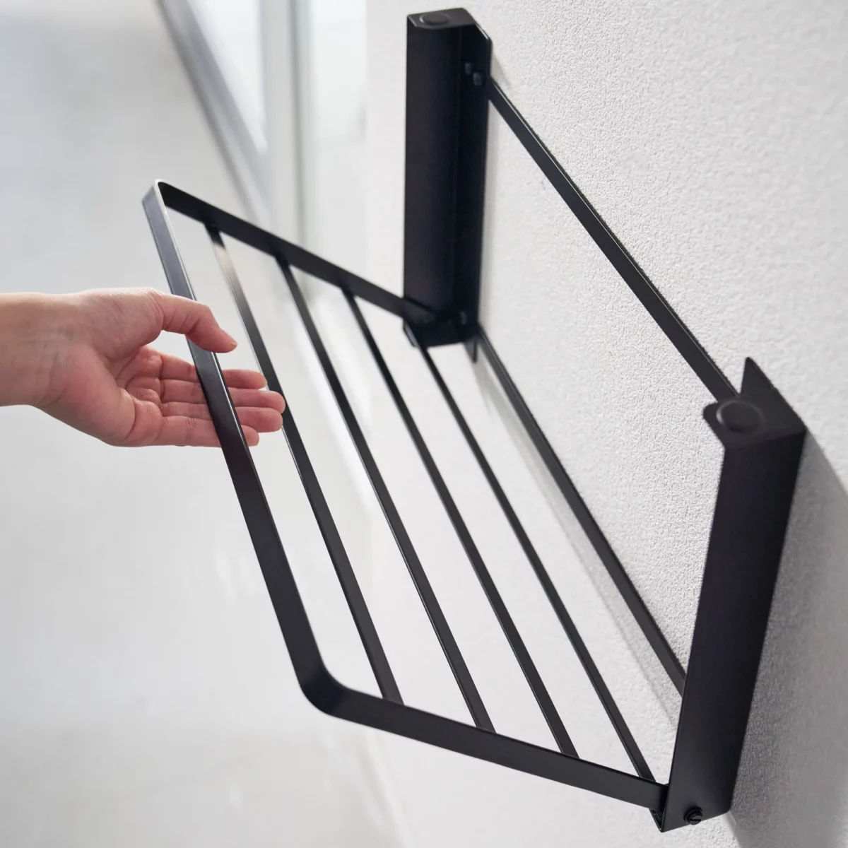 Yamazaki TOWER Folding Wall Shelf in Black; the shelf folds down from the wall by hand