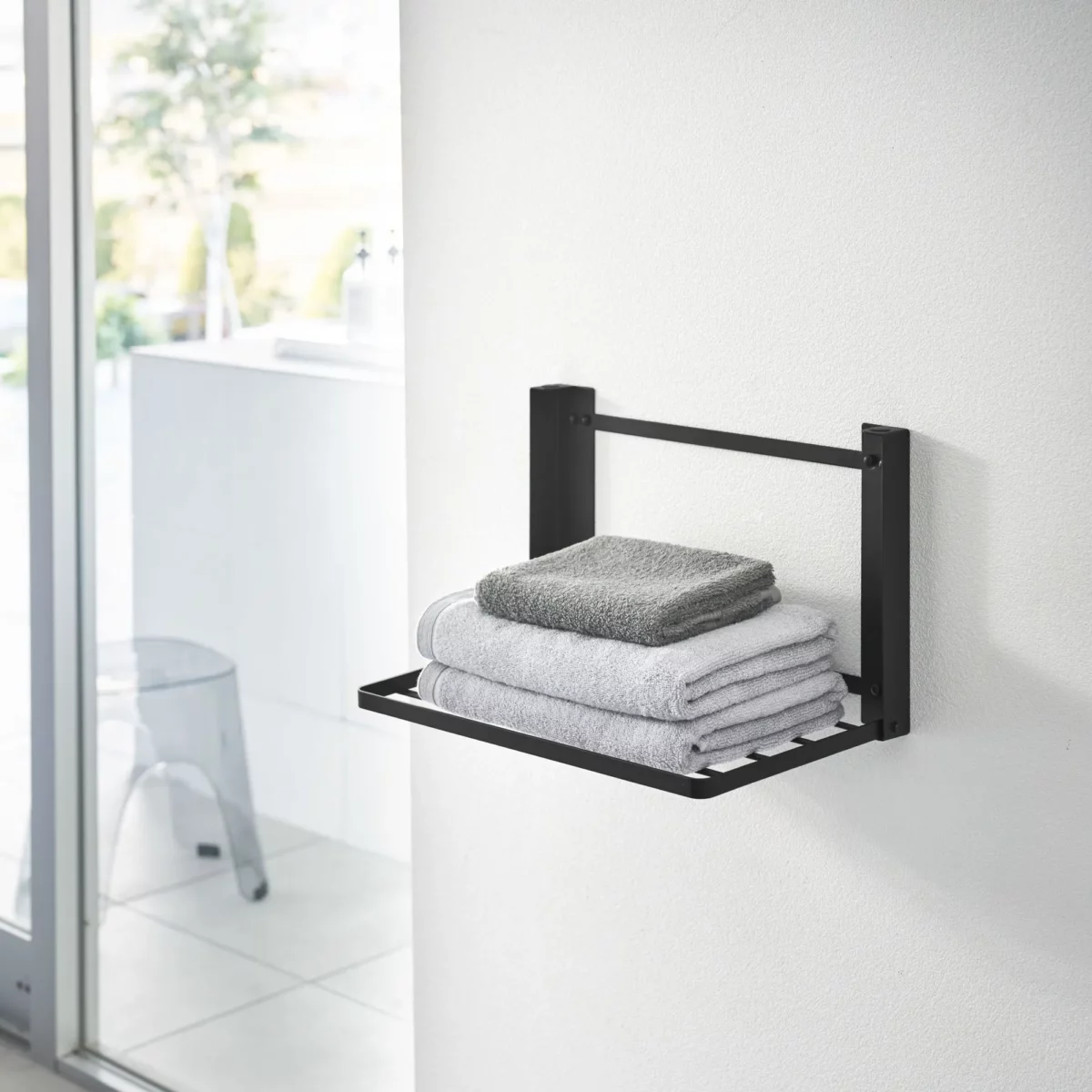 Yamazaki TOWER Folding Wall Shelf in Black, in the bathroom with stacked towels on the shelf