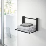Yamazaki TOWER Folding Wall Shelf in Black, in the bathroom with stacked towels on the shelf