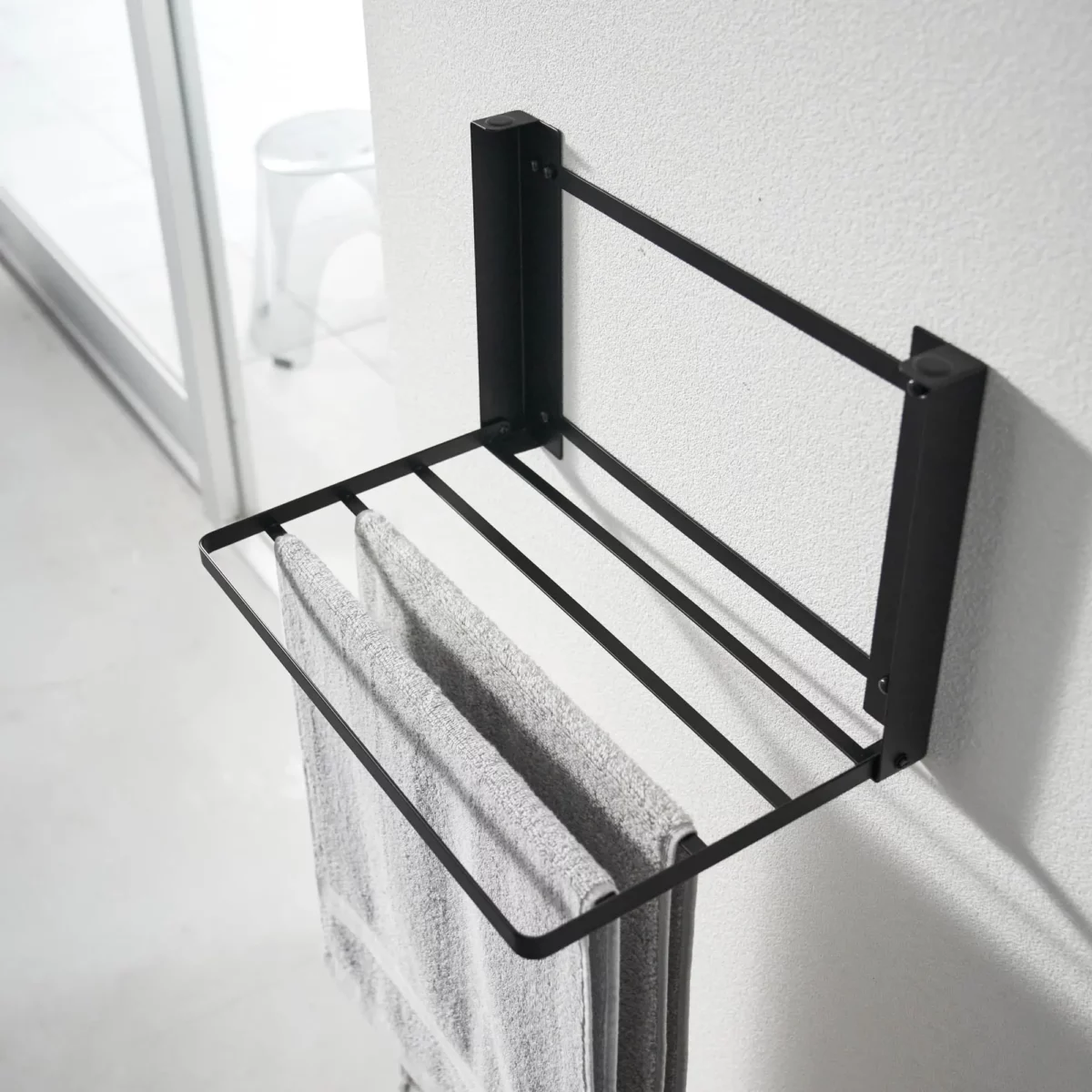 Yamazaki TOWER Folding Wall Shelf in Black; a towel hangs over the supports to dry