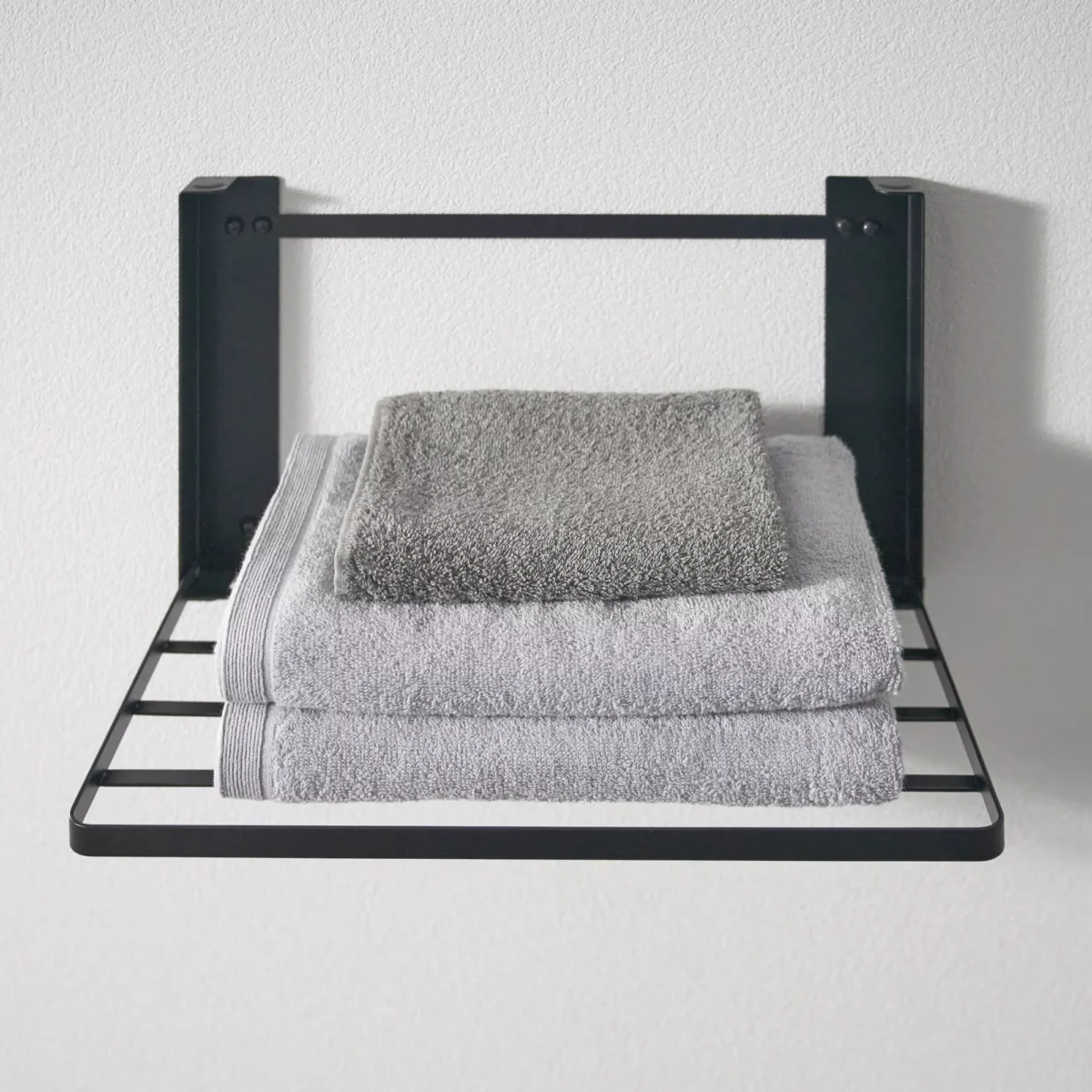 Yamazaki TOWER Folding Wall Shelf in Black, with three folded towels in the foreground
