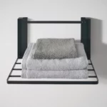 Yamazaki TOWER Folding Wall Shelf in Black, with three folded towels in the foreground