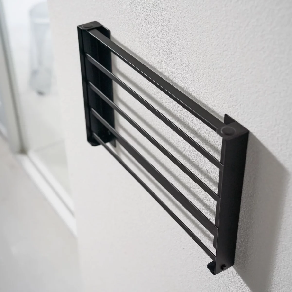 Yamazaki TOWER Folding Wall Shelf in Black, shown folded and mounted on the wall (side view)