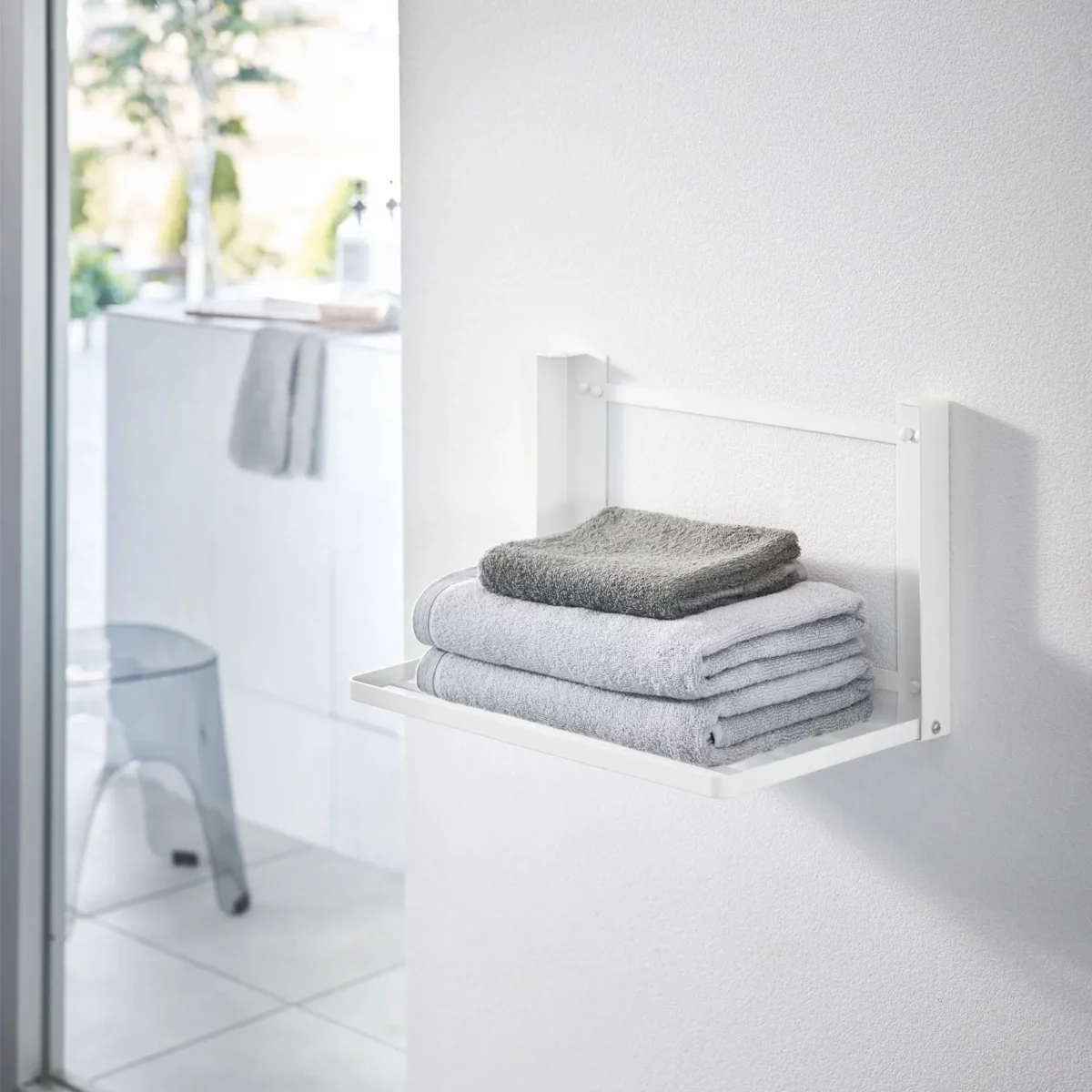 Yamazaki TOWER Folding Wall Shelf in white, in the bathroom with stacked towels on the shelf