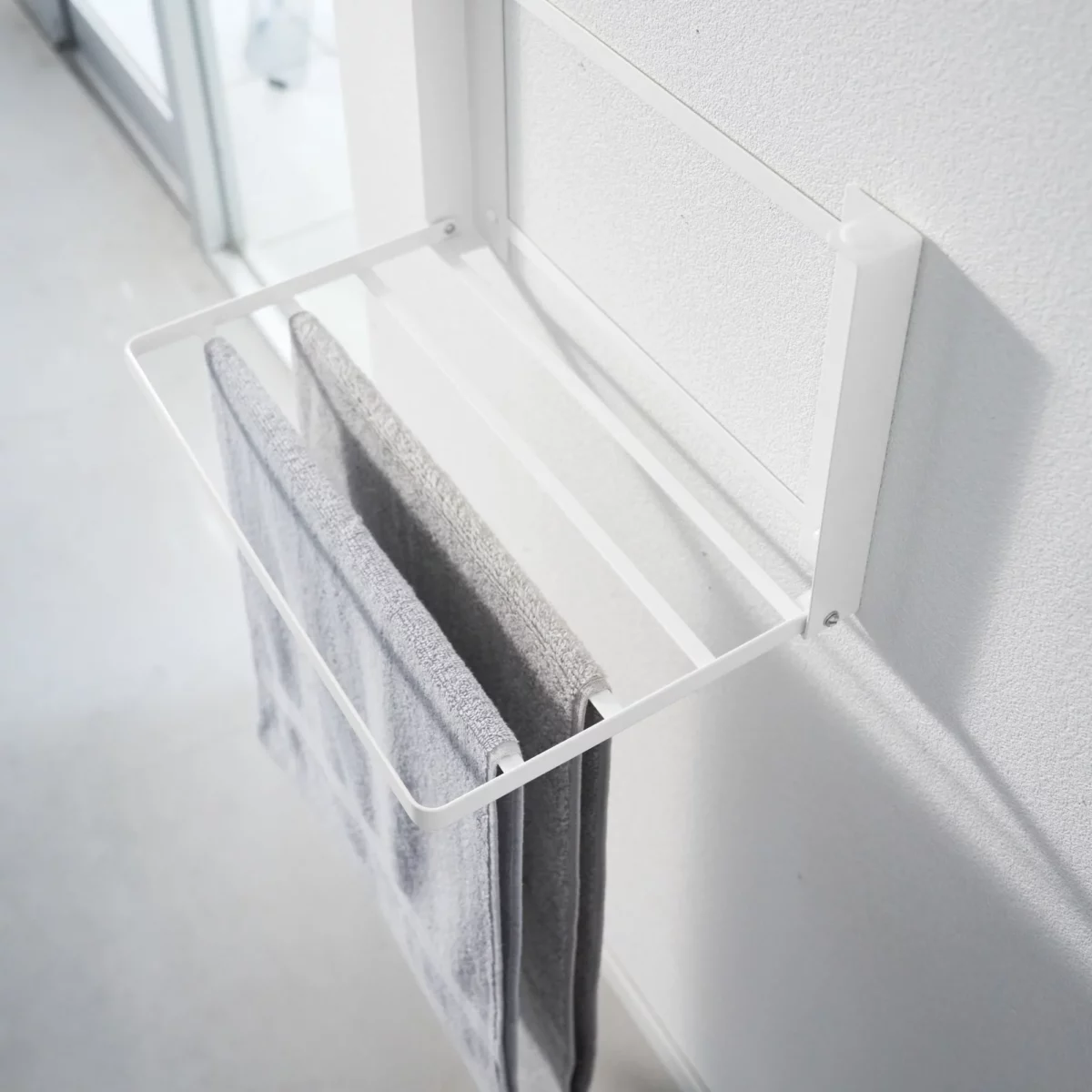 Yamazaki TOWER Folding Wall Shelf in White; a towel hangs over the supports to dry