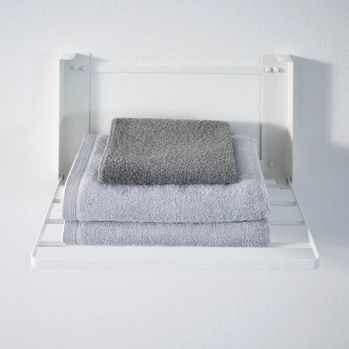 Yamazaki TOWER Folding Wall Shelf in White, with three folded towels in the foreground
