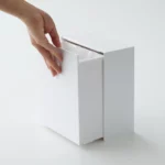 Boîte à crochets adhésifs Yamazaki TOWER avec couvercle, de couleur blanche, posée sur la tablette, le couvercle s'ouvre à la main