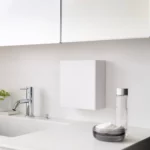 Boîte à crochets adhésifs Yamazaki « TOWER » avec couvercle, de couleur blanche, fixée au mur au-dessus du lavabo
